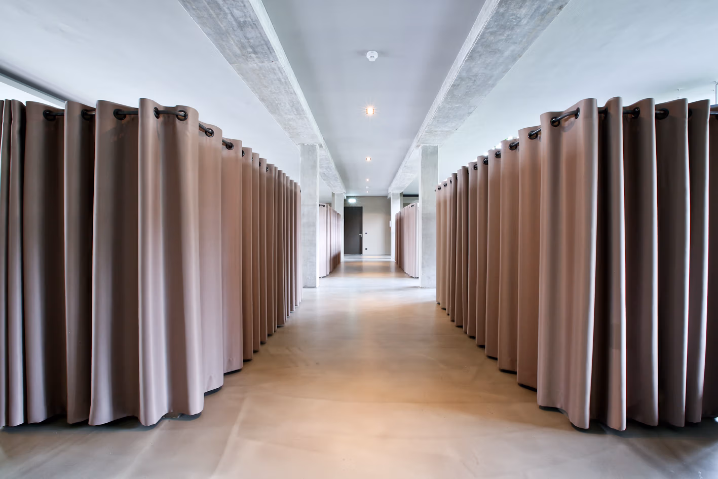 Innenausbau mit raumteilendem Vorhangsystem, Betonflächen und reduziertem Textilkonzept.